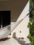 Hammock hanging outside a house with shoes on the floor and plants nearby
